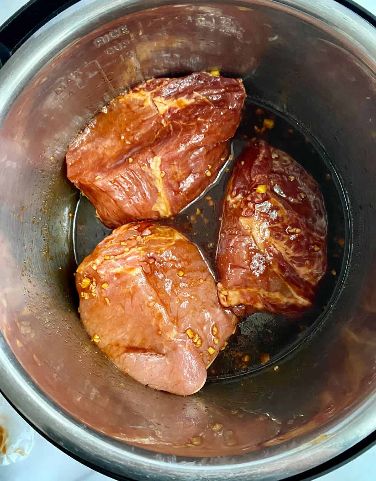 A raw pork loin cut into 3 pieces, loaded in a slow cooker and topped with sauce.
