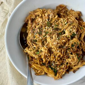 A bowl of cooked Slow Cooker Asian Pulled Pork with a spoon.