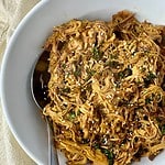 A bowl of cooked Slow Cooker Asian Pulled Pork with a spoon.