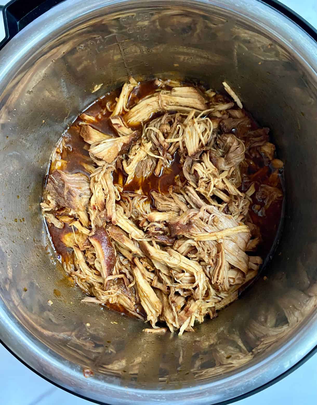 A slow cooker with cooked shredded pork sitting in sauce.