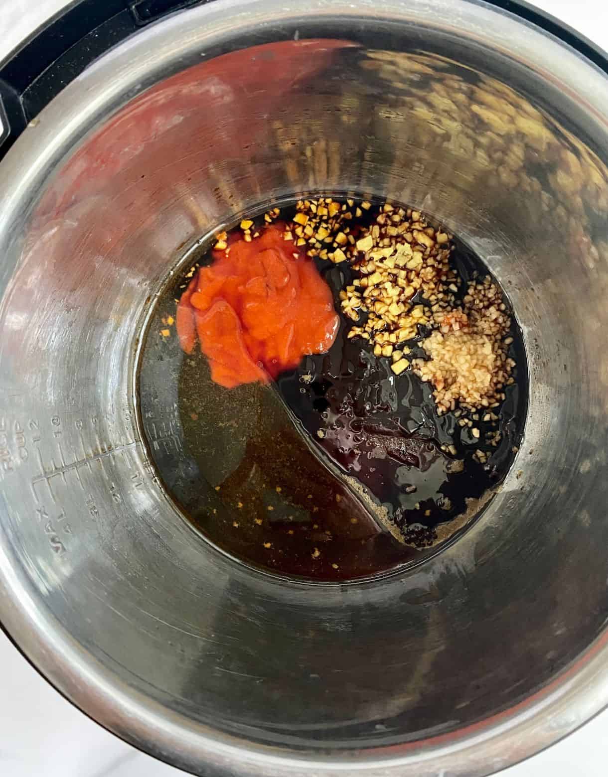 A slow cooker with soy sauce, sriracha sauce, hoisin sauce, brown sugar, ginger and garlic added but not stirred.