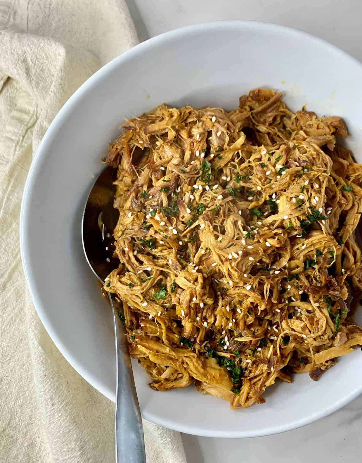 A bowl of cooked Slow Cooker Asian Pulled Pork with a spoon.