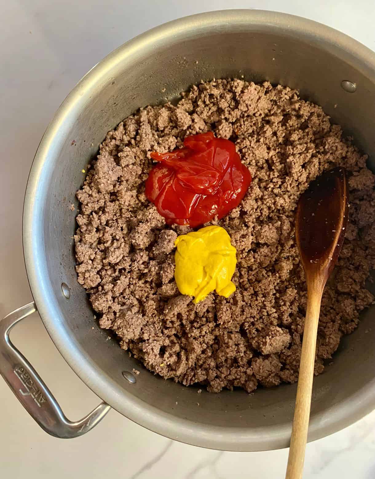 A pot of cooked burger bowl beef with globs of ketchup and mustard on top.