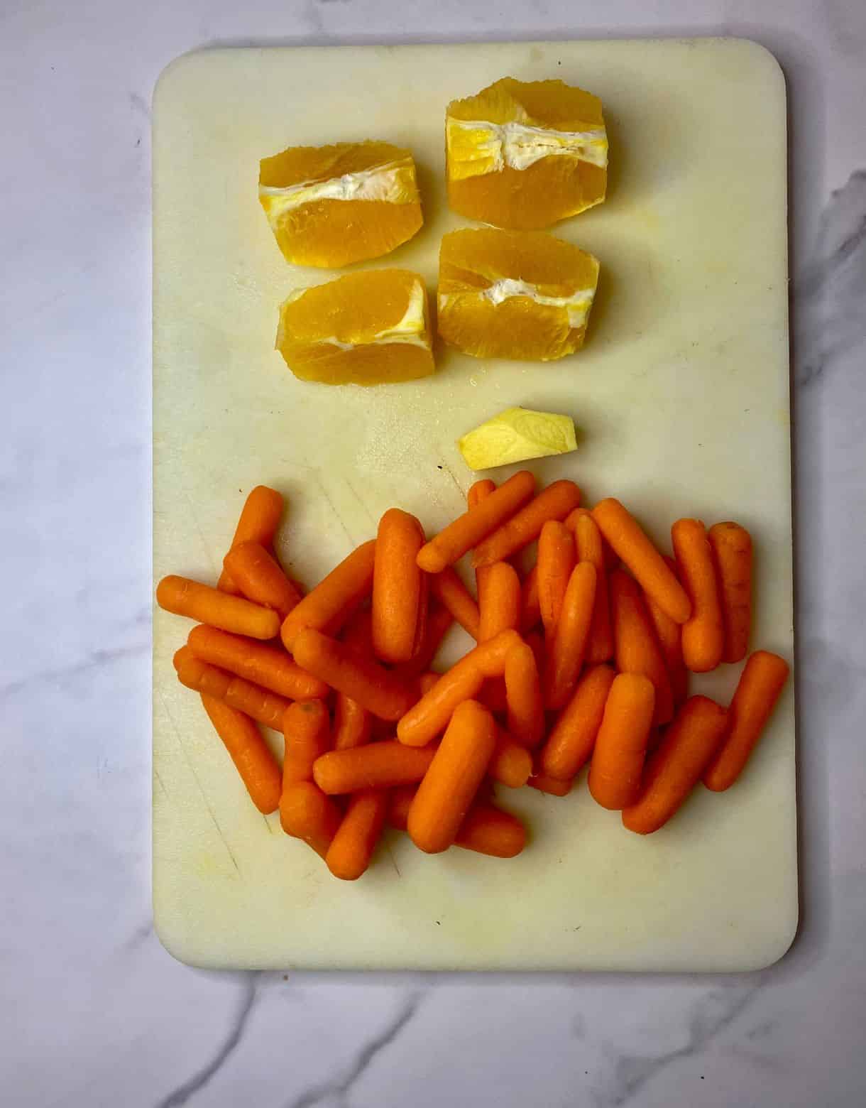 Peeled carrots, peeled chunk of ginger, an orange peeled and quartered on a cutting board.