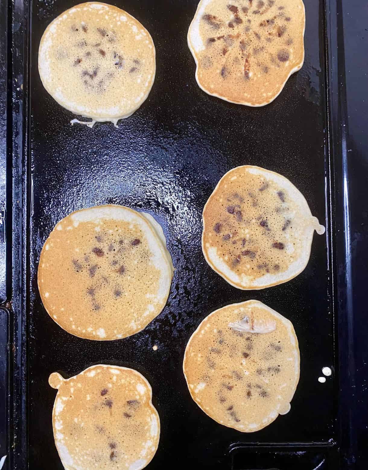 Chocolate Chip Pancakes on the griddle with a browned and cooked top.