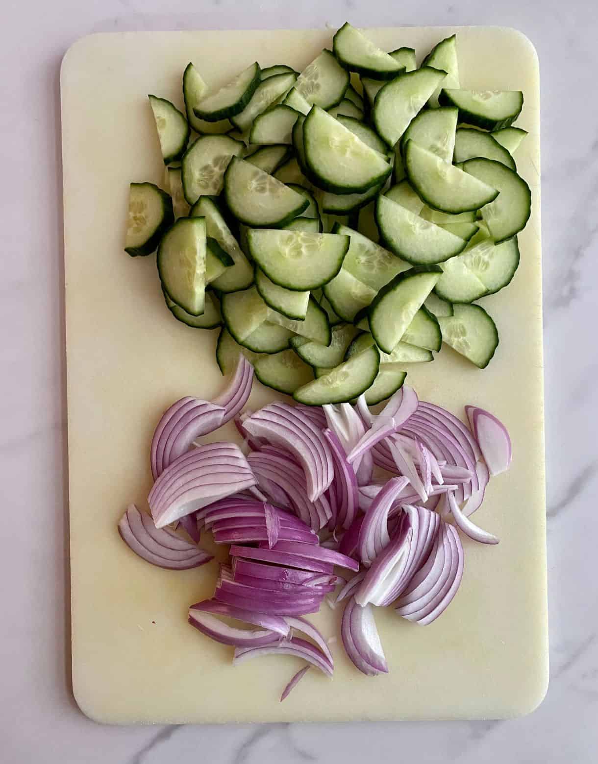 Sliced onions and chopped cucumbers on a cutting board.