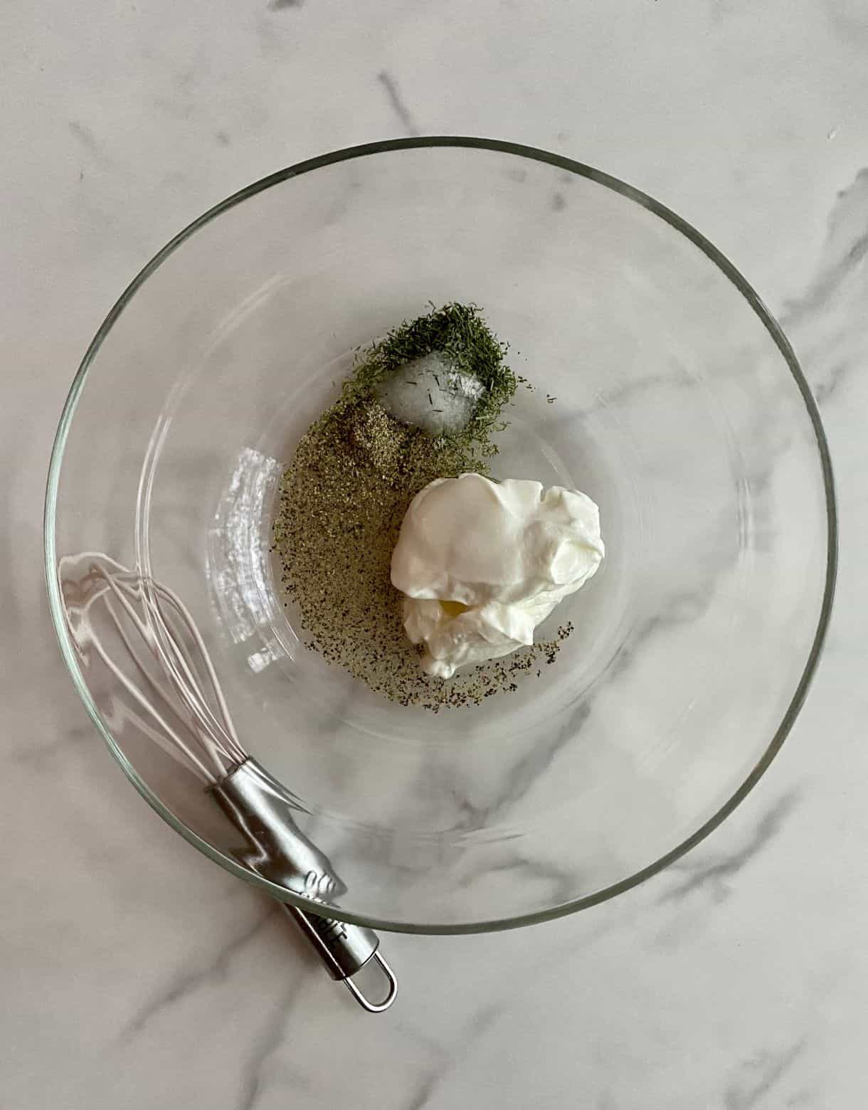 A bowl with sour cream, vinegar, salt, pepper and dill and a whisk.
