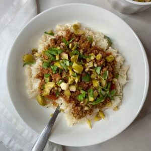 A bowl of Filipino Picadillo with cauliflower rice and spiced meat topped with chopped olives and cilantro.