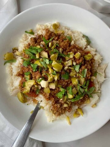 A bowl of Filipino Picadillo with cauliflower rice and spiced meat topped with chopped olives and cilantro.