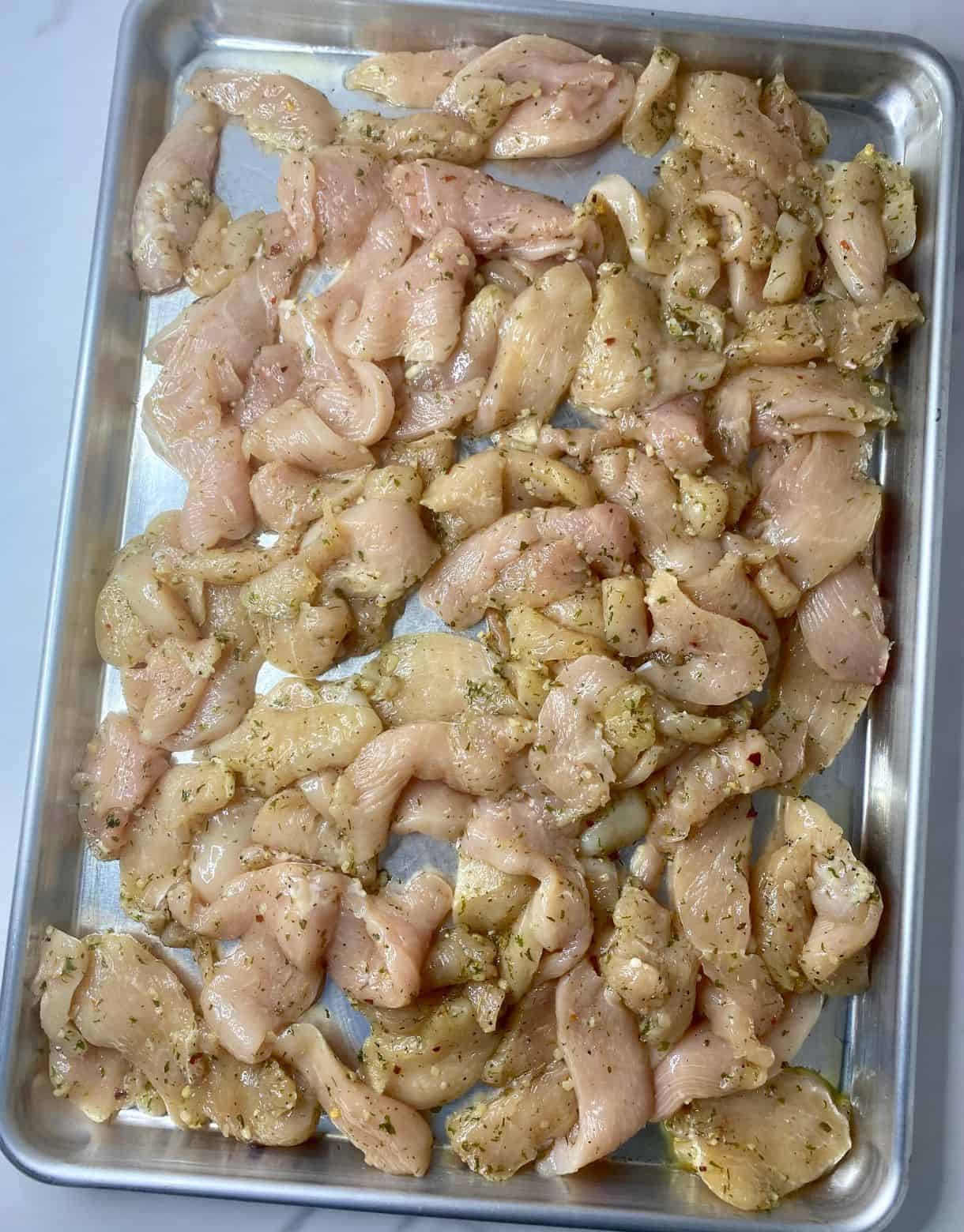 Sheet Pan with raw seasoned Mediterranean Chicken.