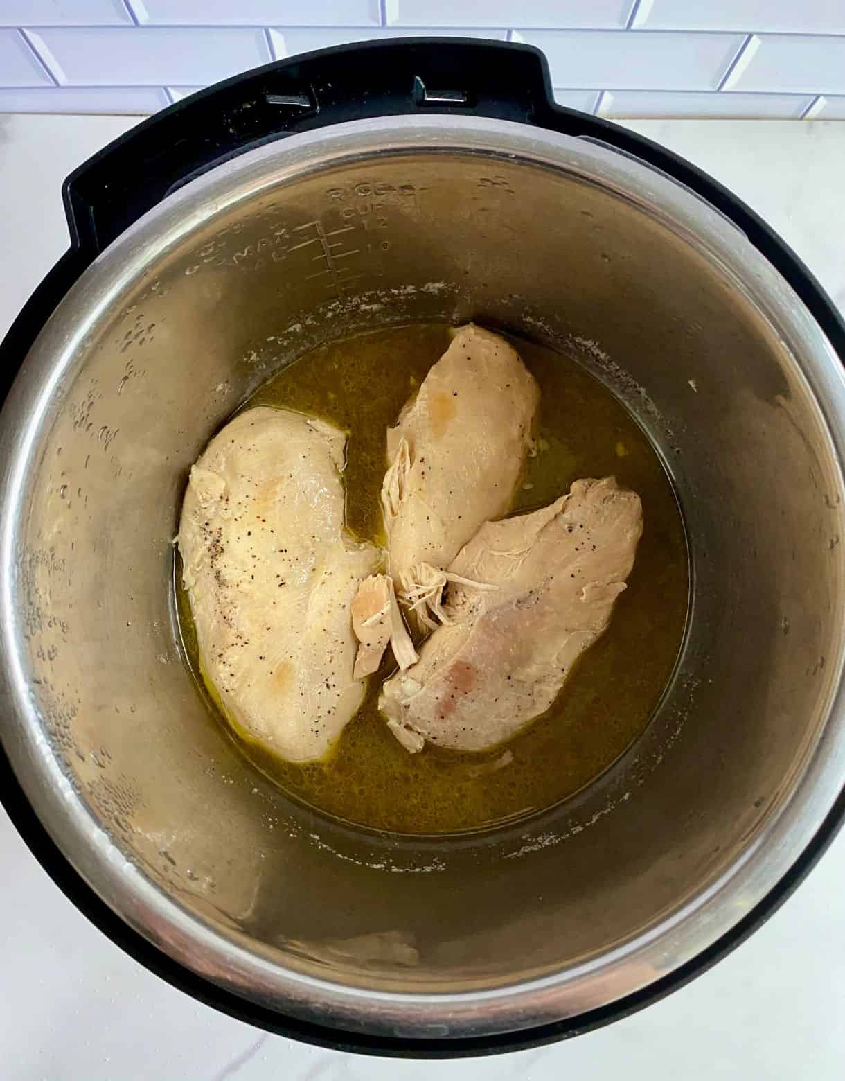 A slow cooker with 3 cooked chicken breasts.