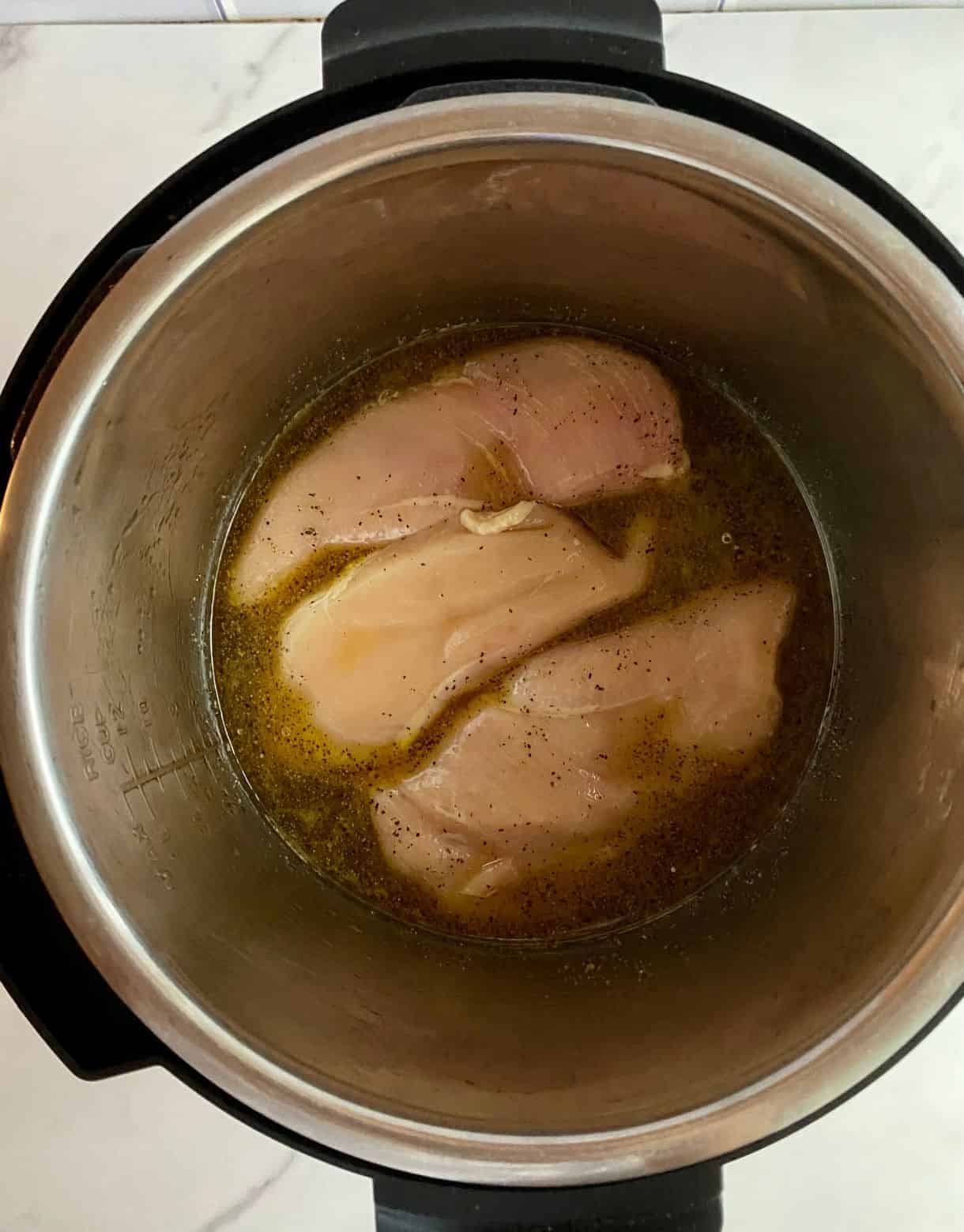 A slow cooker with 3 raw chicken breasts.