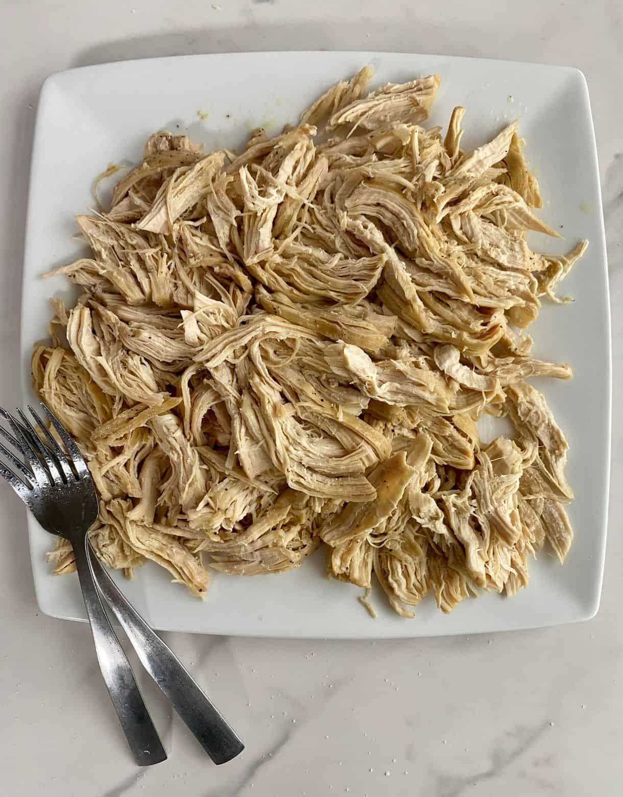 A plate of cooked shredded chicken breast and two forks.