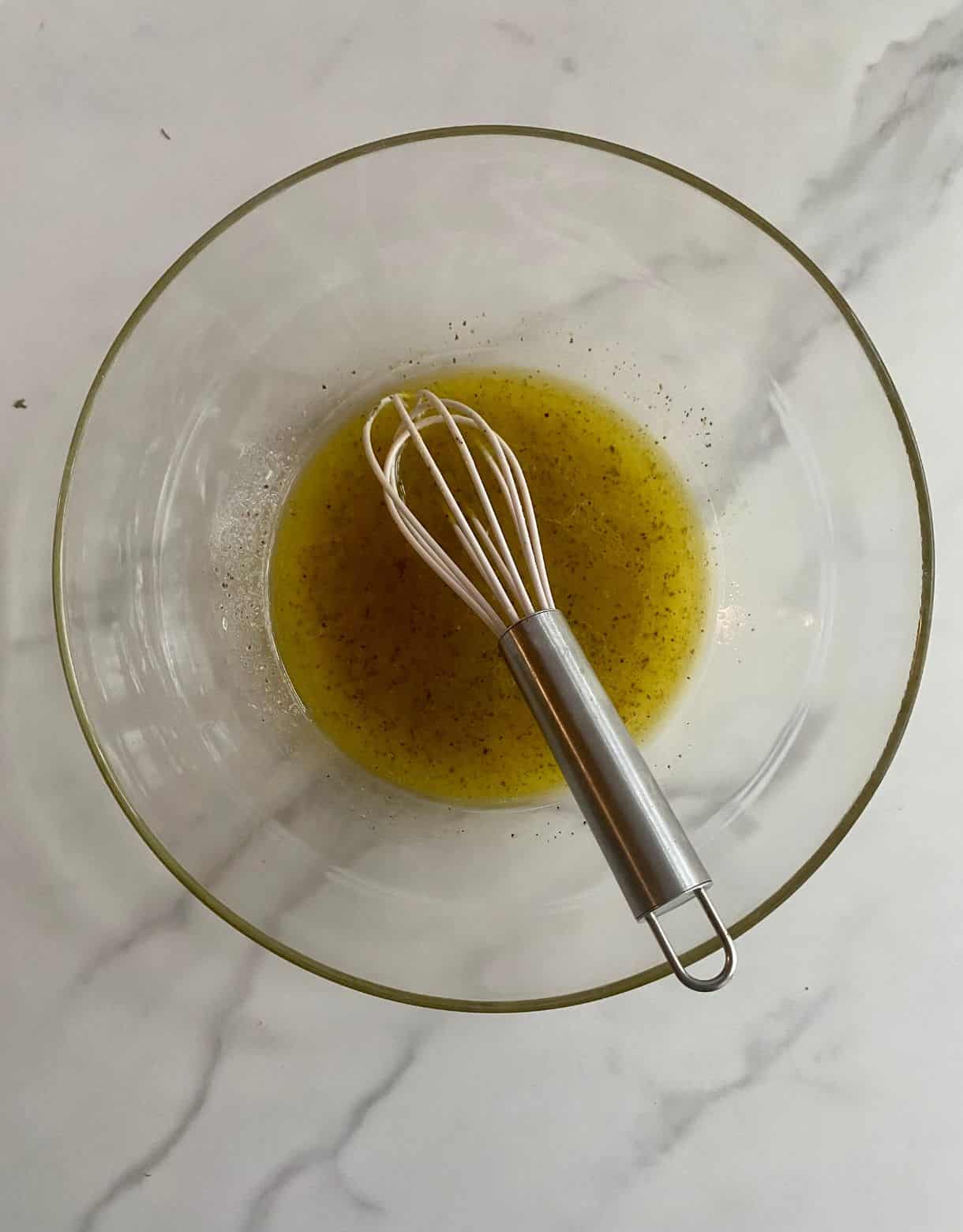 A bowl with a whisk with lemon juice, olive oil, salt and black pepper added to the bowl.