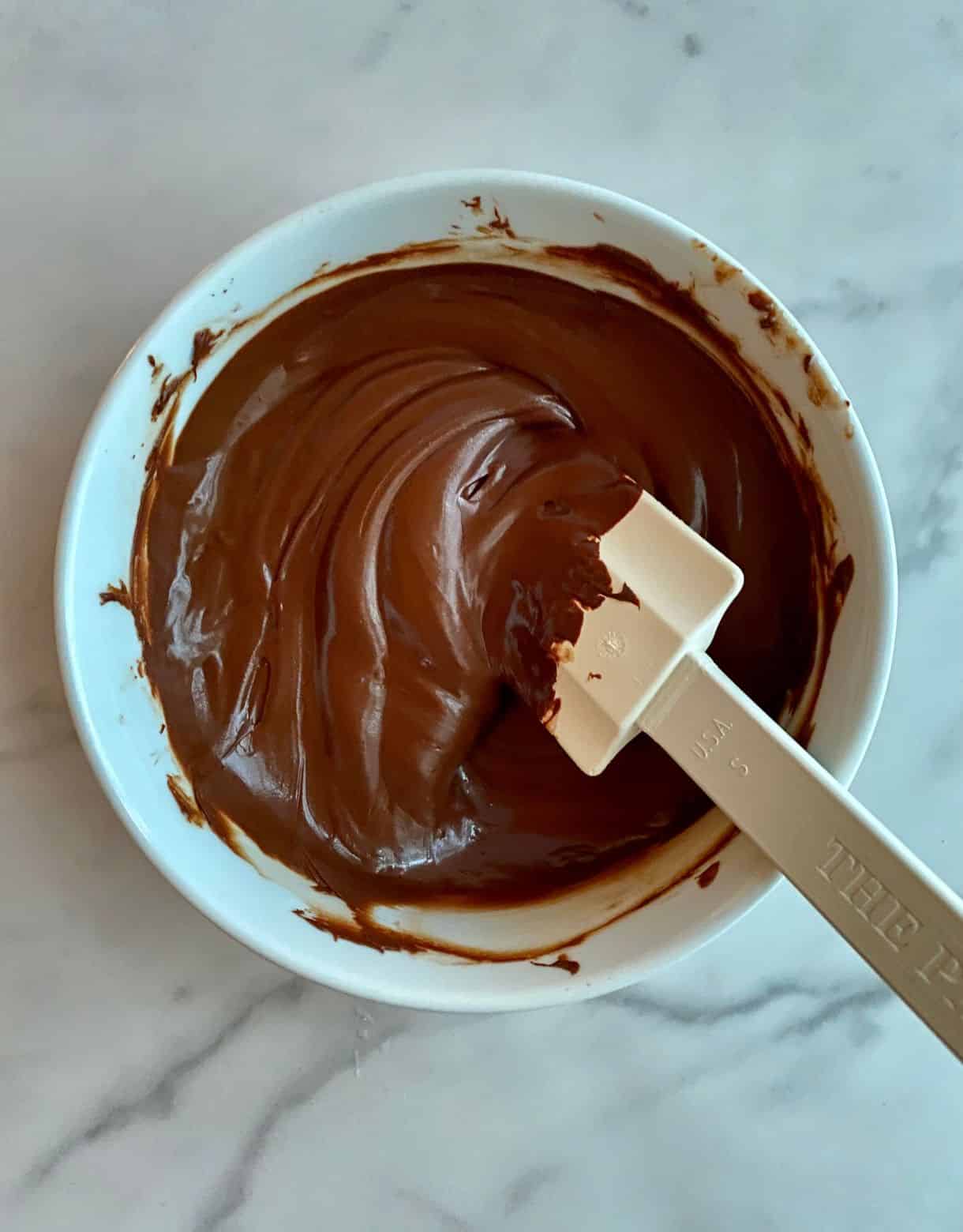 A bowl of melted chocolate with a spatula.