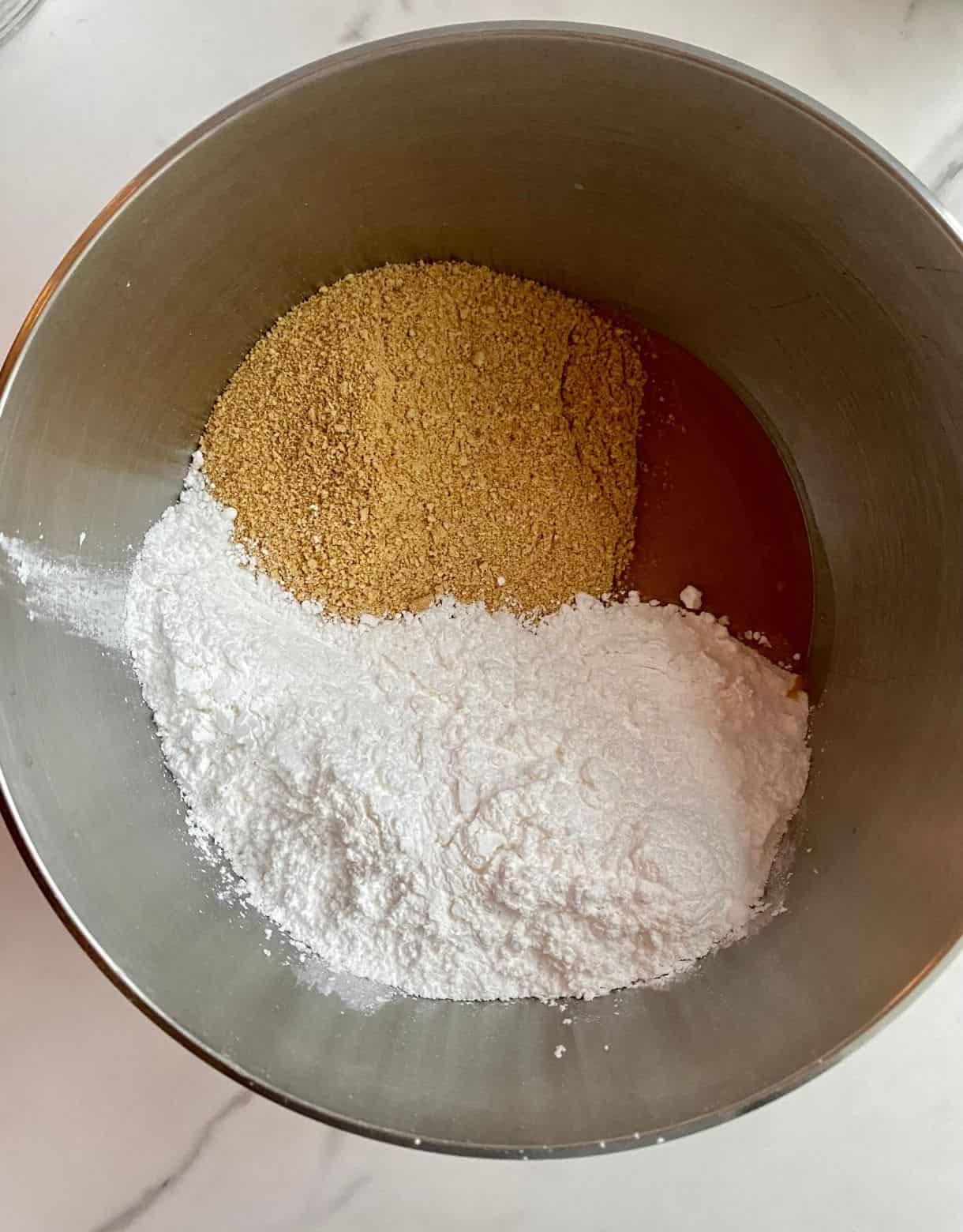 A mixing bowl with powdered sugar, graham cracker crumbs and melted butter and peanut butter.