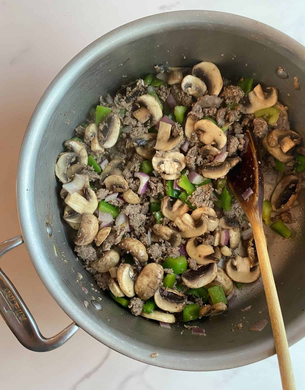 Cooked sausage, mushrooms, onions and peppers in a pot.