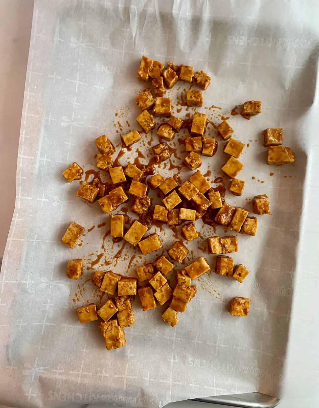 Marinated Sesame Tofu spread on a sheet pan lined with parchment to be baked.