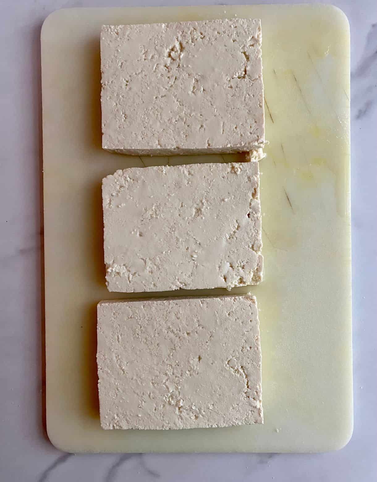 A cutting board with tofu sliced into 3 slabs.