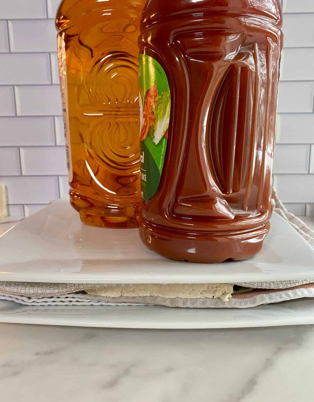 Slabs of tofu wrapped in towels, pressed between two plates and weighted with gallon drinks.