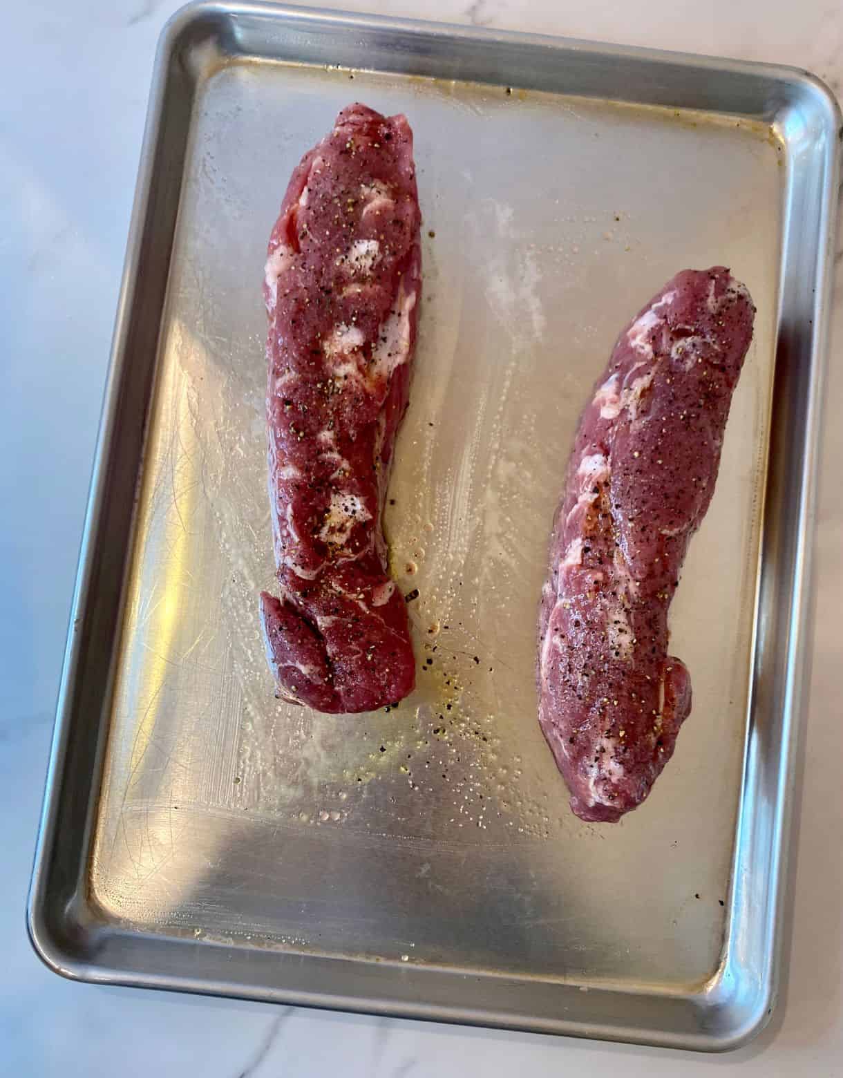 Two raw pork tenderloins on a sheet pan.