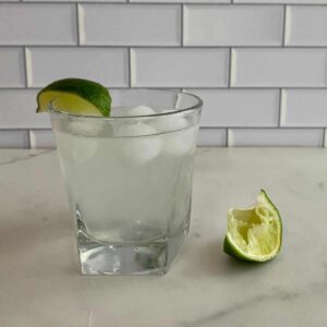 A glass of Skinny Cocktail with ice and a lime wedge.