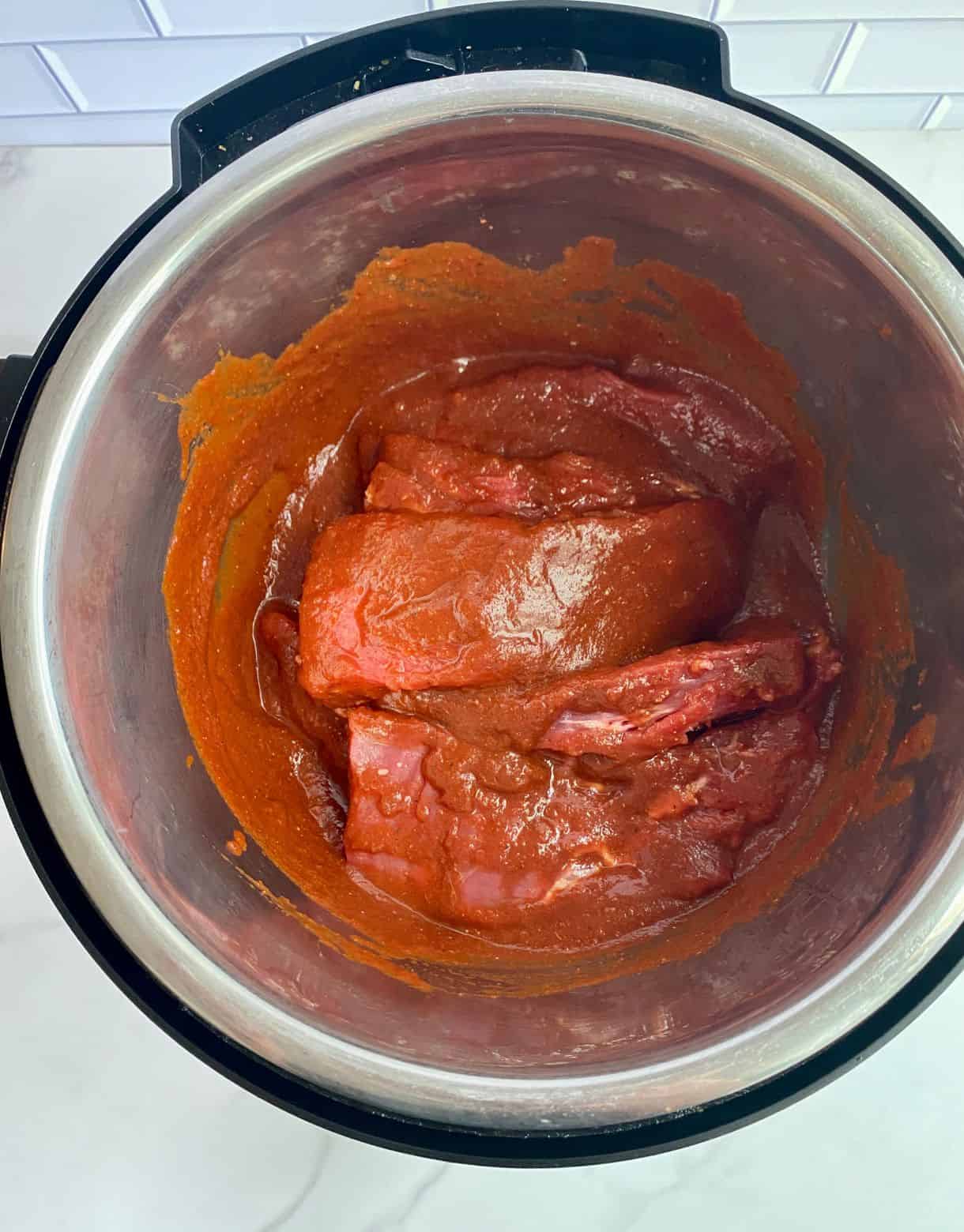A slow cooker with raw beef and sauce for Pulled Beef Tacos.