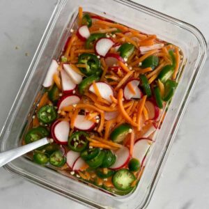 A container of Vietnamese Pickled Vegetables with sliced jalapenos, sliced radishes and shredded carrots floating in vinegar.