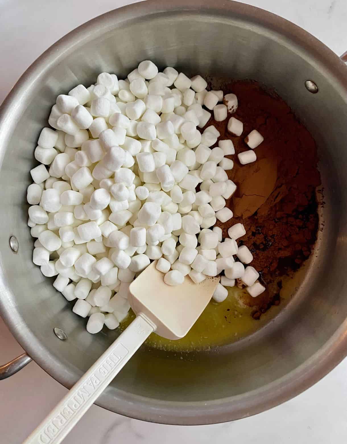 A pot with melted butter and cocoa powder and mini marshmallows added but not stirred.