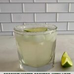 A Coconut Water Cocktail in a glass with a wedge of lime and a salted rim.