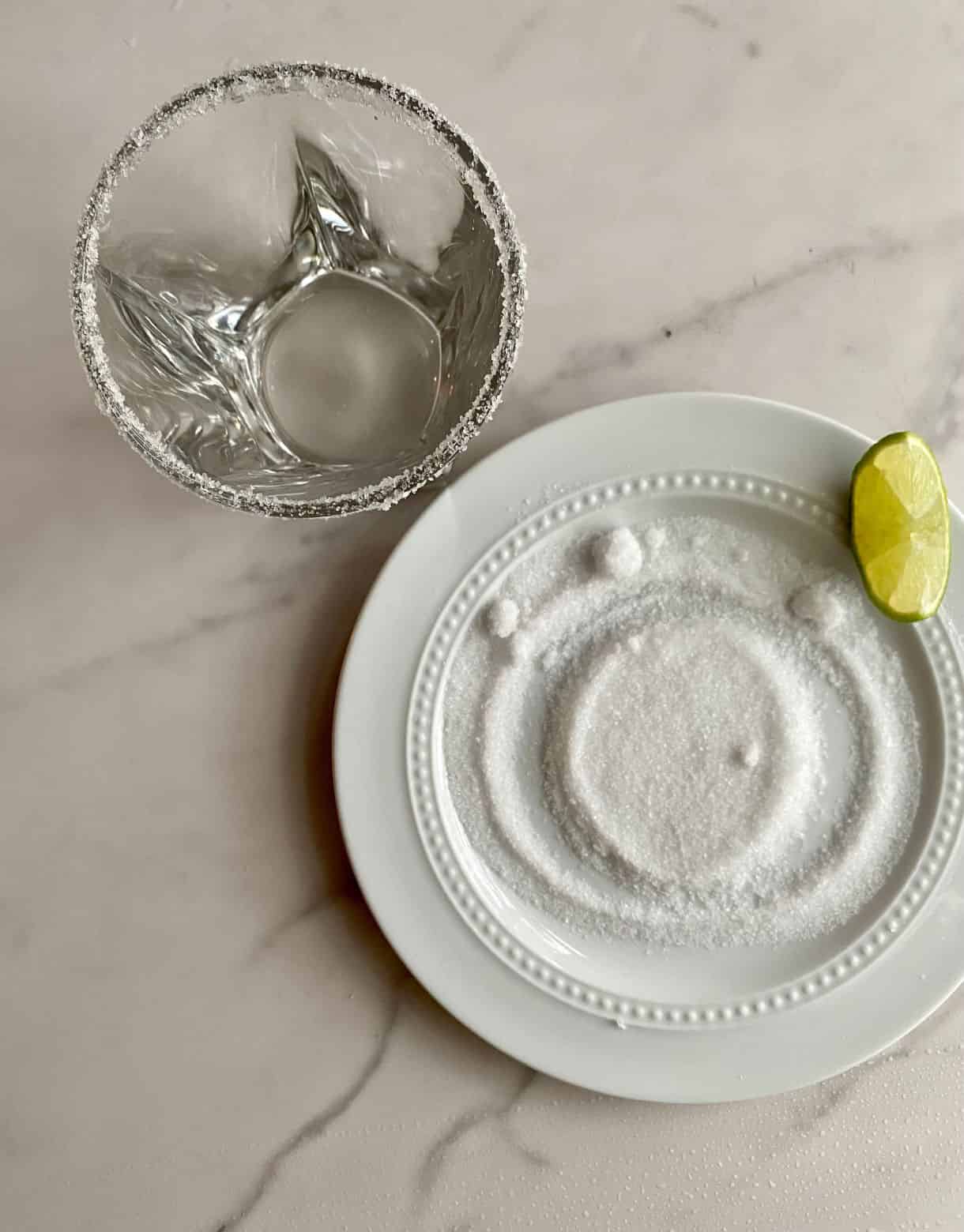 A plate of salt with a wedge of lime and a glass with a salted rim ready to make a Coconut Water Cocktail.