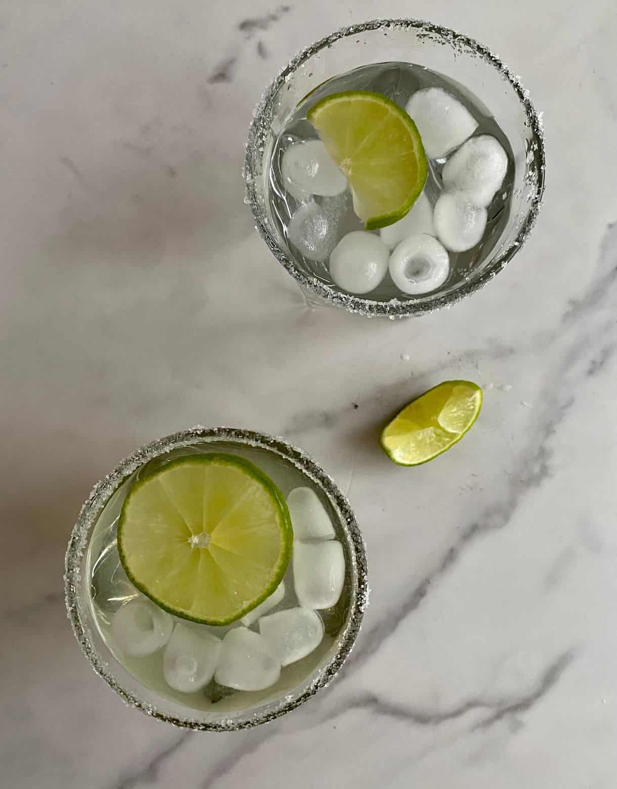Two glasses of Coconut Water Cocktail with ice, lime wedges and salted rims.