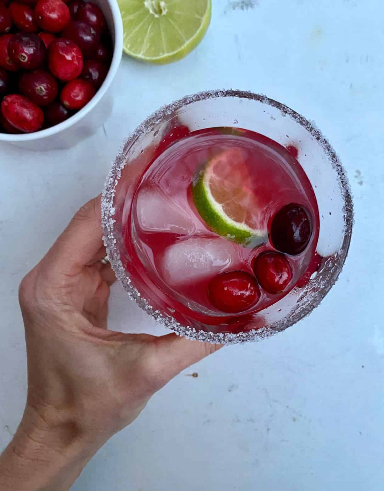 A hand holding a glass of Cranberry Margarita with a salted rim.