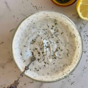 A bowl with Yogurt Dill Sauce and a spoon for serving.