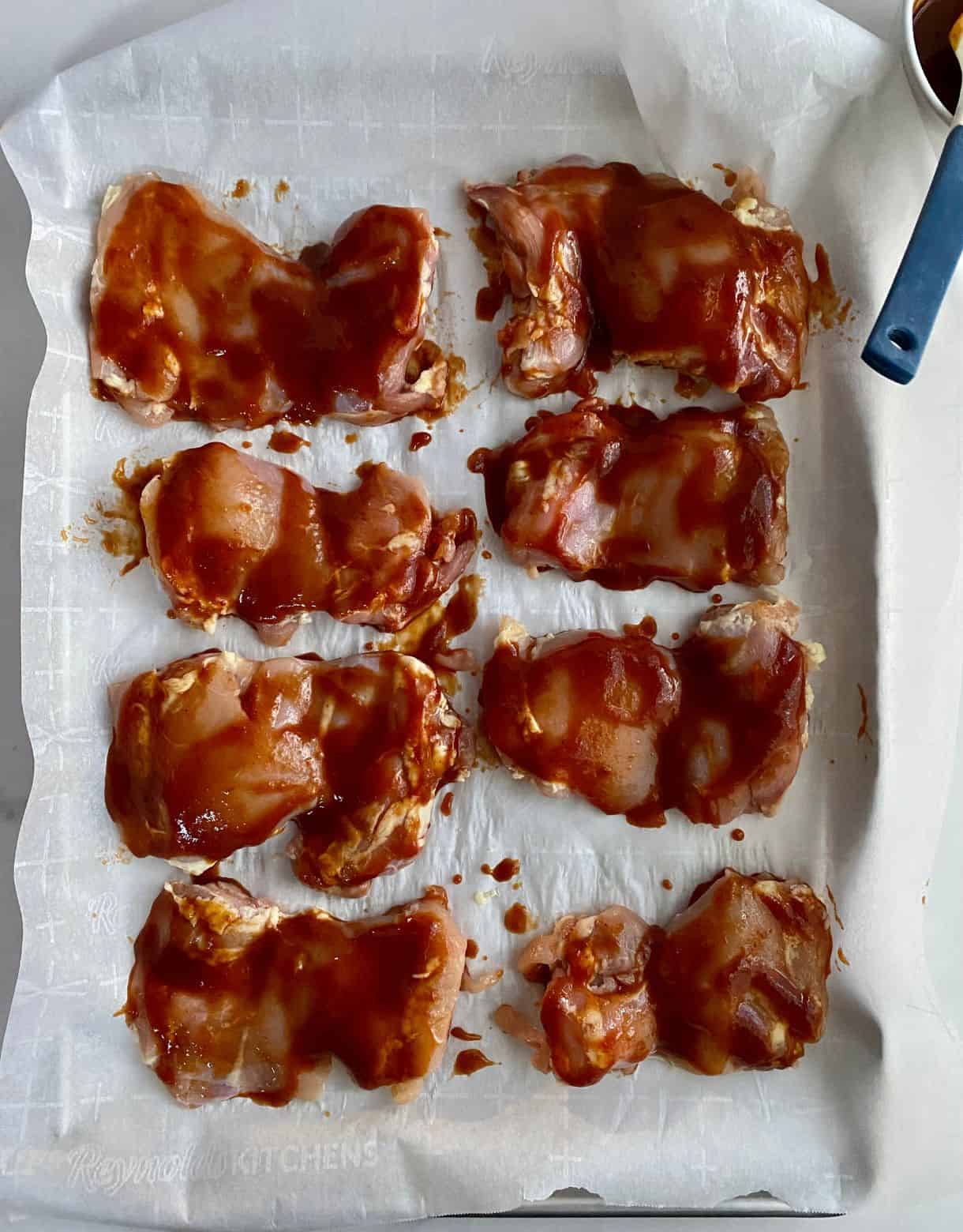 A sheet pan with raw chicken thighs brushed with BBQ Sauce.
