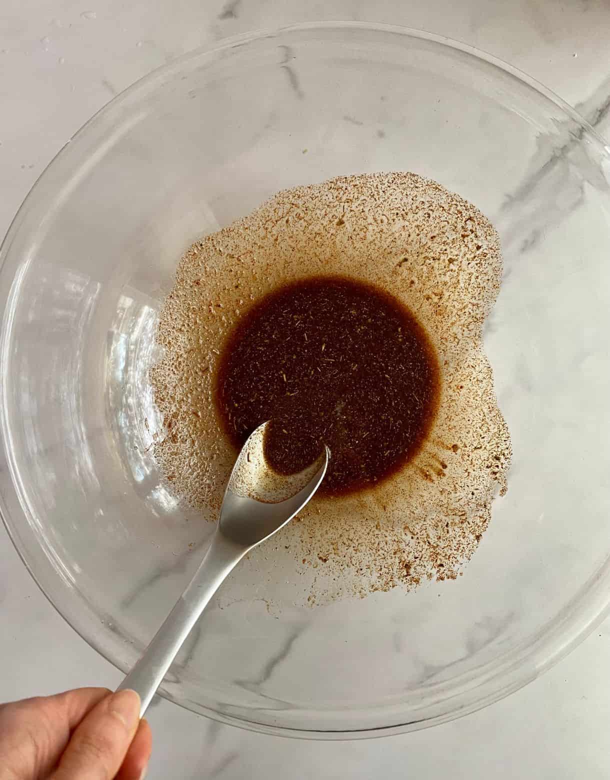A bowl with olive oil stirred with spices and a spoon.