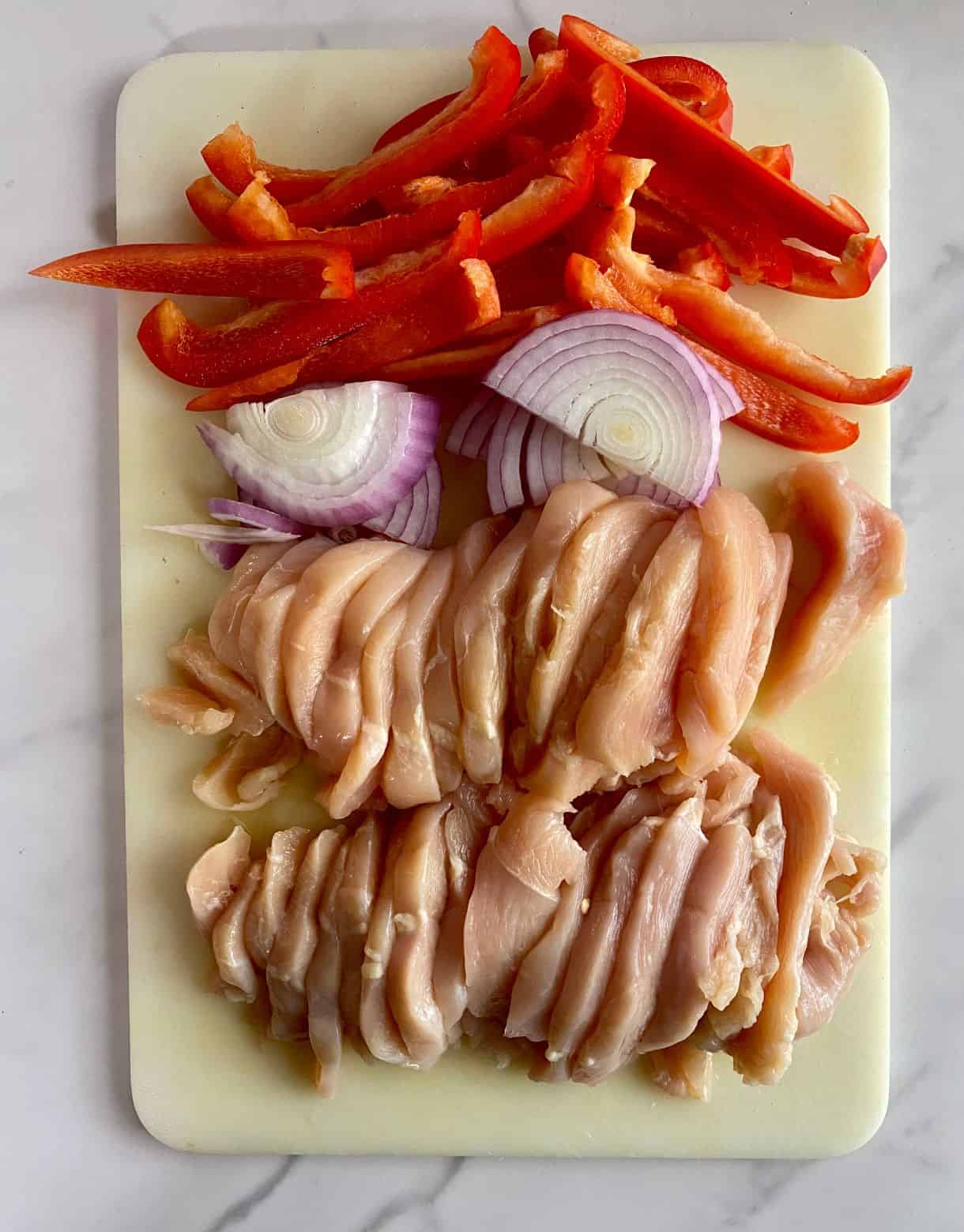 A cutting board with sliced chicken, onions and bell pepper.
