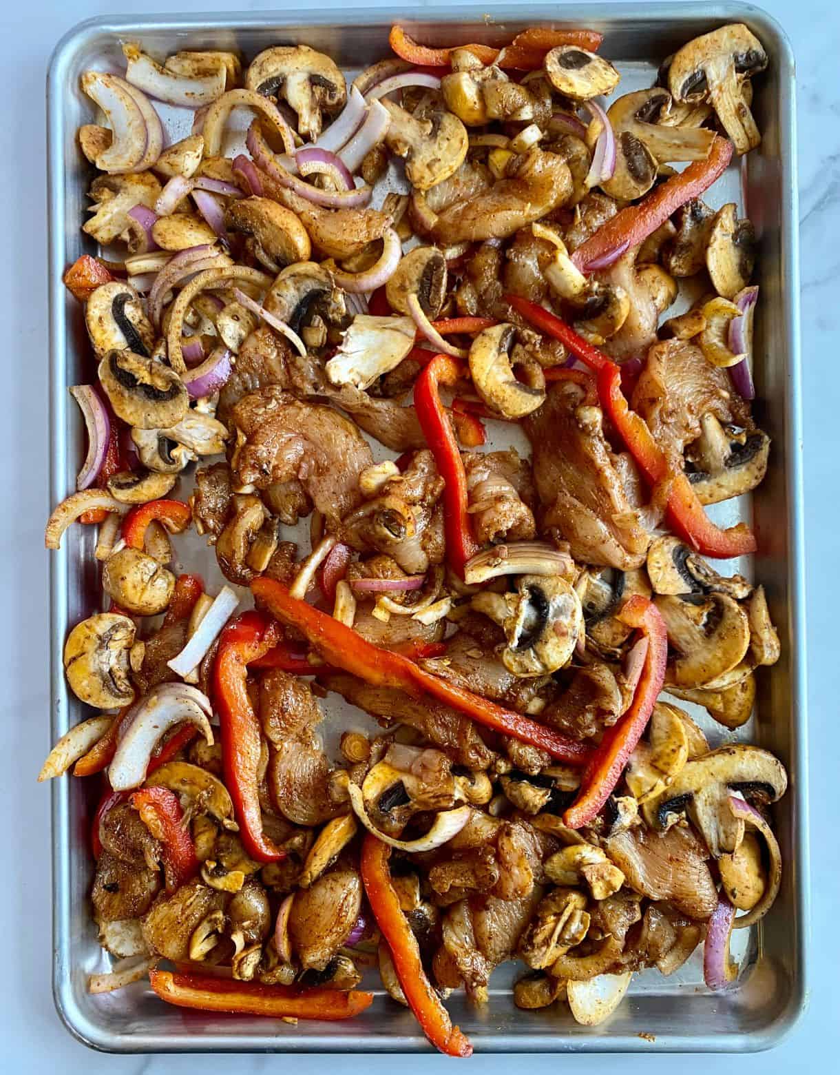 A sheet pan with uncooked Chicken Fajita Tray Bake.
