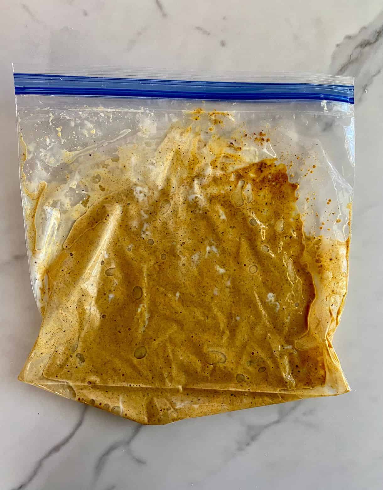 A ziploc freezer bag with yogurt, lemon juice, garlic and spices added and squished to mix.