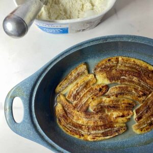 A dish with baked Healthy Bananas Foster and a tub of vanilla ice cream with a scoop in it.