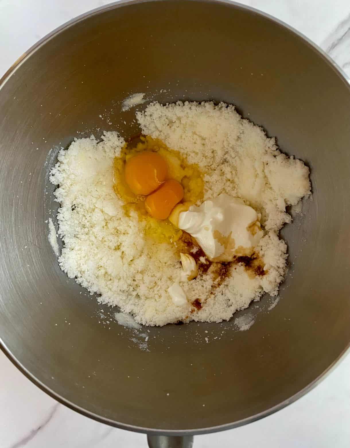 A bowl with creamed butter and sugar with eggs, yogurt and vanilla added but not mixed.