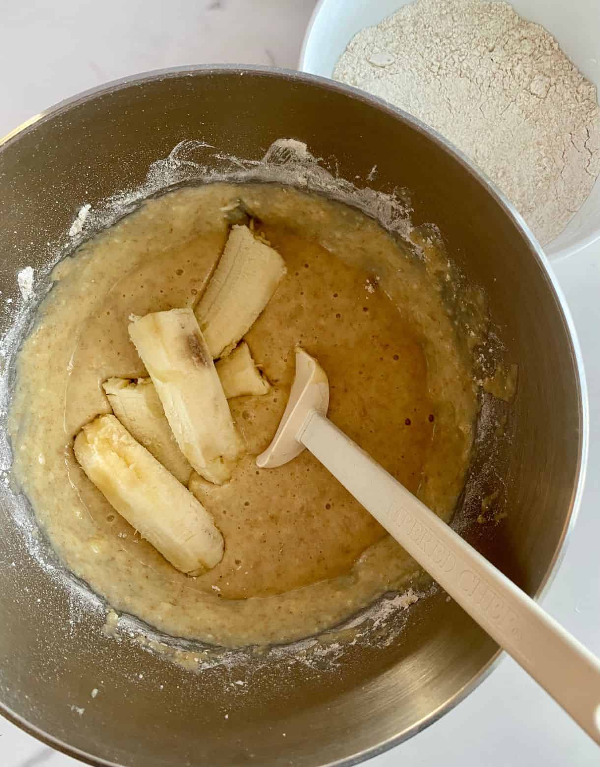 A bowl with batter for Healthy Chocolate Chip Banana Muffins with bananas added but not mixed.