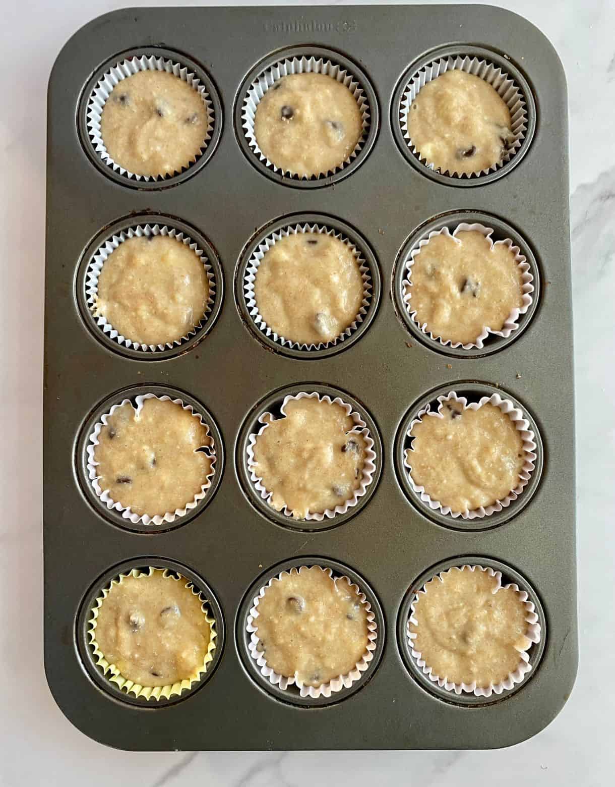 A muffin pan with muffin lines and batter added for Healthy Banana Chocolate Chip Muffins.