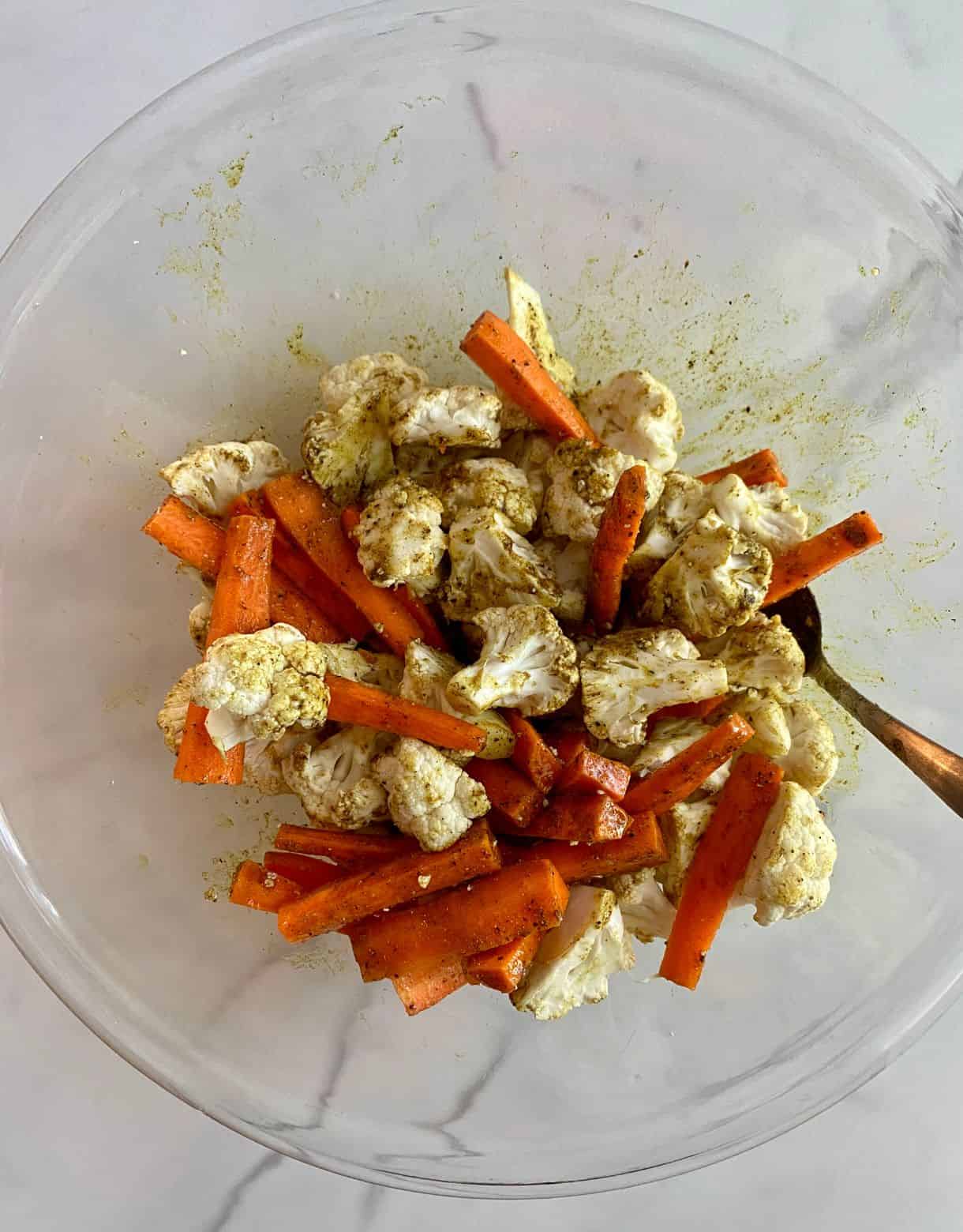 A bowl with cauliflower and carrots tossed with oil and spices.