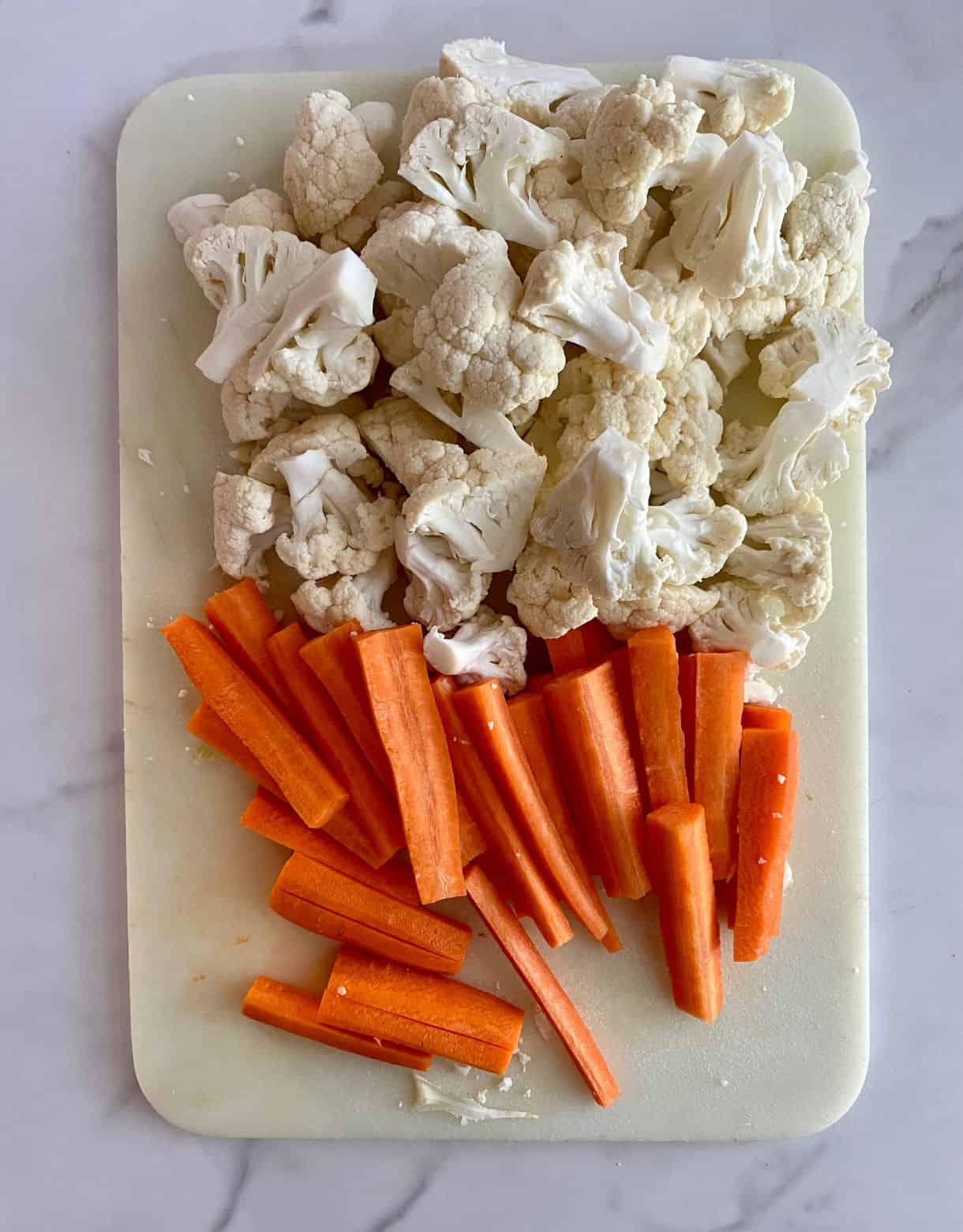 A cutting board with chopped raw cauliflower and carrots.