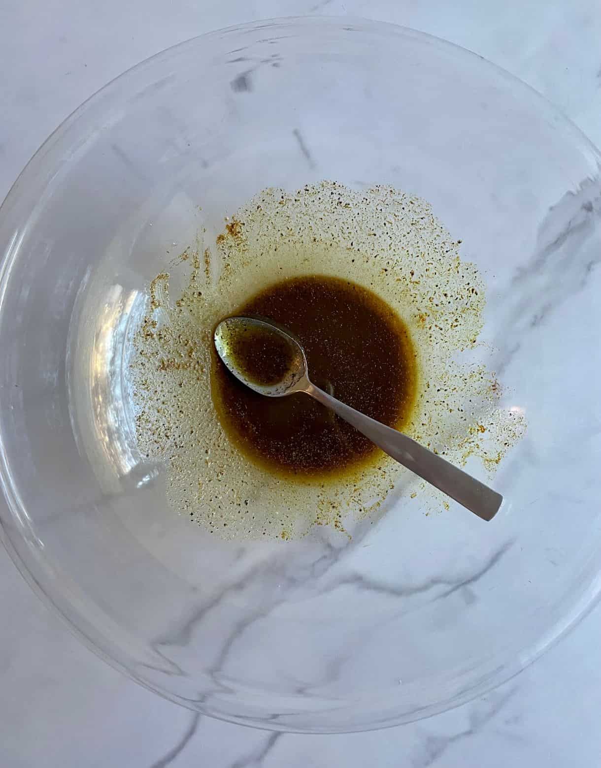 A bowl with olive oil, salt and pepper stirred together and a spoon.