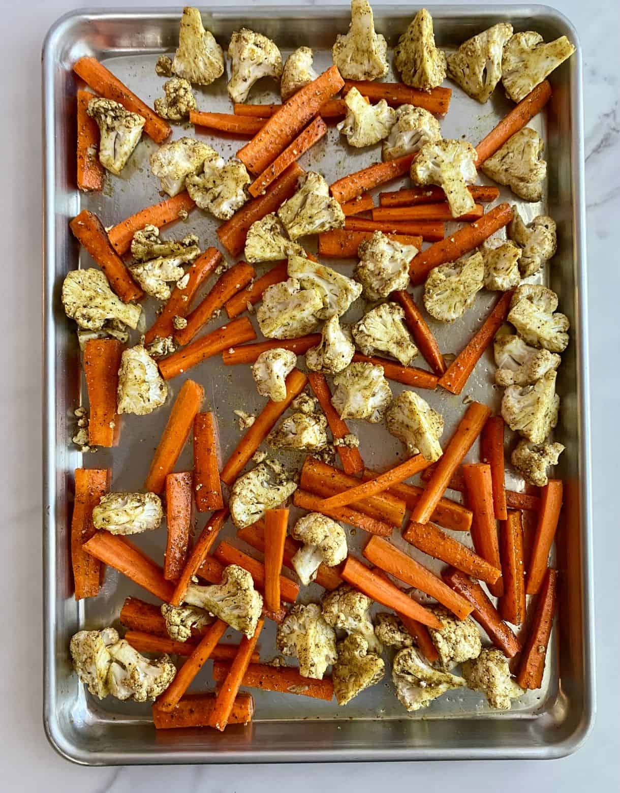 A sheet pan with raw seasoned cauliflower and carrots on it.