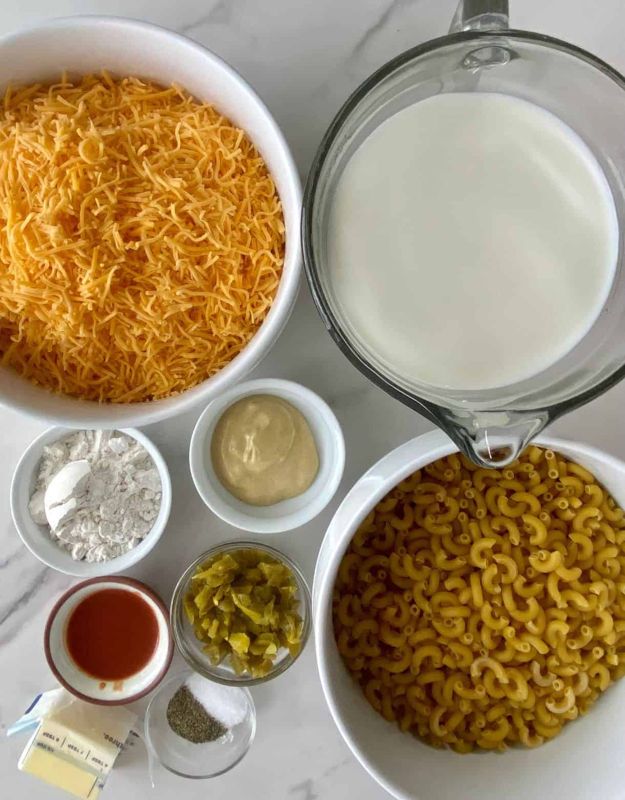 Ingredients for Jalapeno Mac and Cheese. Shredded cheddar cheese, milk, macaroni noodles, flour, dijon mustard, diced jalapenos, hot sauce, butter, salt and pepper.