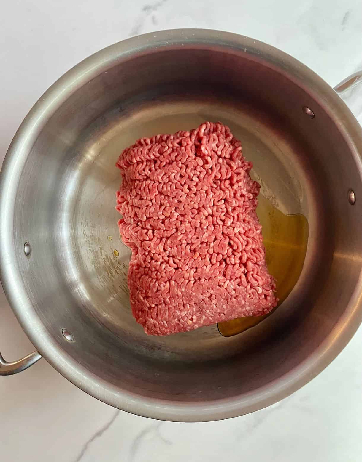 A skillet with sesame oil and raw ground beef.