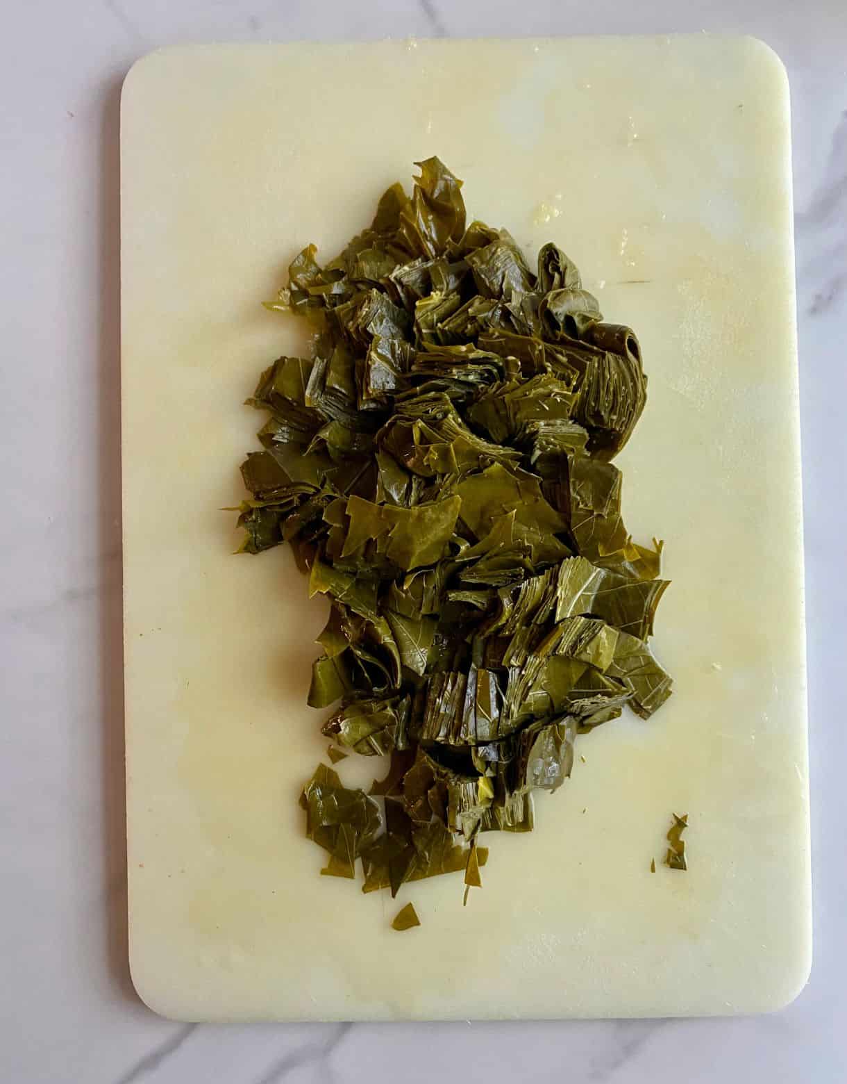 A cutting board with a pile of chopped grape leaves.